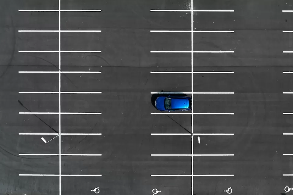 Bird's eye view of empty asphalt parking lot with one blue car.